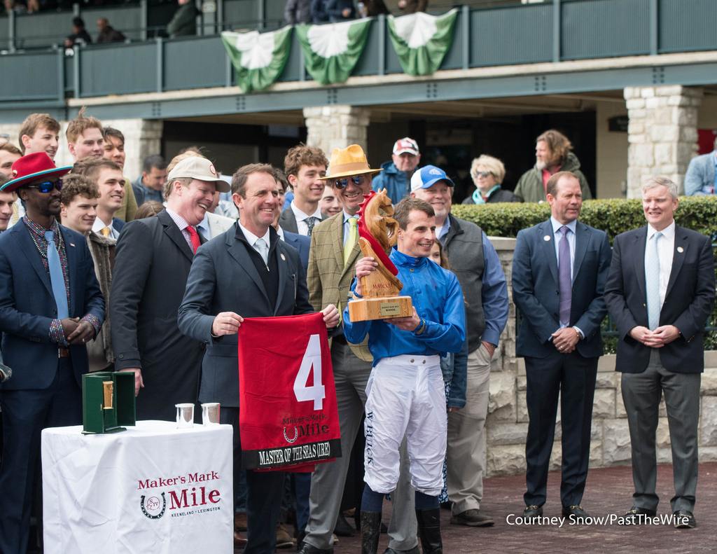 Jockey William Buick hoists the very large trophy. (Courtney Snow/Past The Wire)