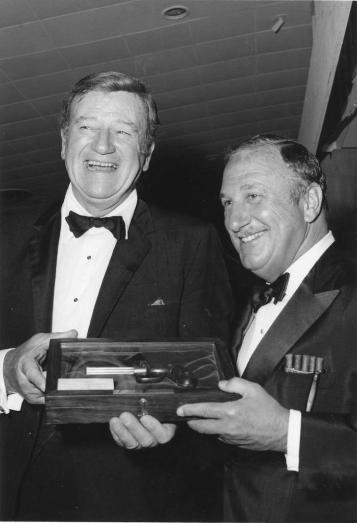 Chapman College Challenge '70 Dinner, held at the Balboa Bay Club, Newport Beach, California, September 18, 1970. Mr. Wayne and Trustee Clement L. Hirsch, a co-sponsor of the banquet, admire one of two antique pistols presented to the actor from the collection of the late J. E. Wilkinson, former Chairman of the Chapman Board. (Chapman University Events Collection)